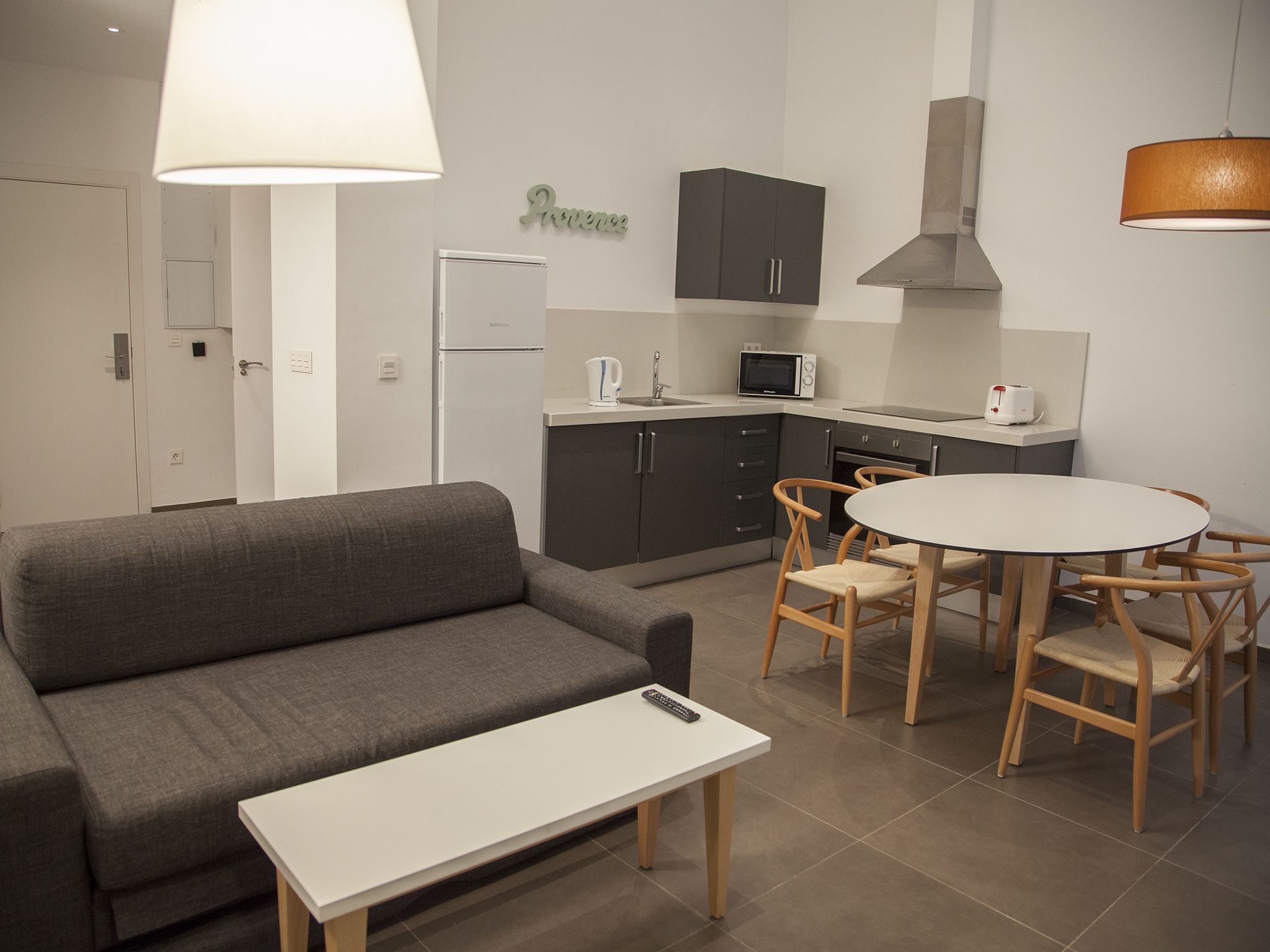 A compact living space with a sofa, a dining table with chairs, a kitchenette, and a lamp.