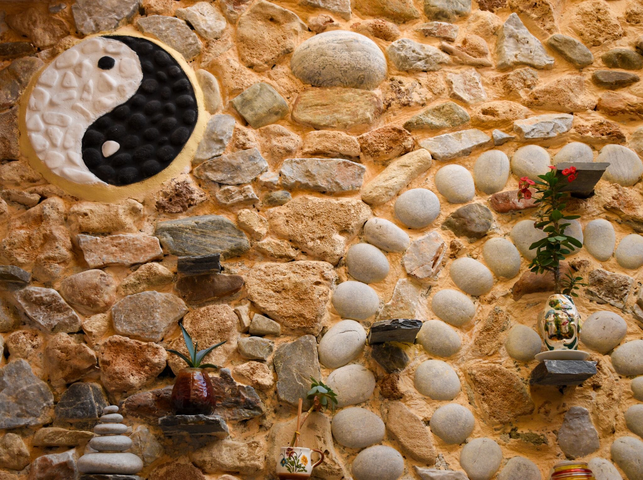 Un mur de pierres orné d’un symbole yin et yang, ainsi que de divers rochers et de petites plantes.