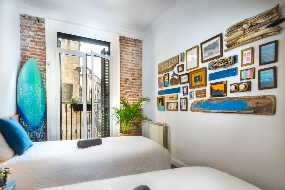 Quarto com duas camas, uma prancha de surf e uma parede decorada com várias fotos emolduradas e uma placa.