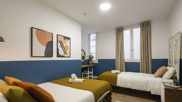 A hotel room with two beds, a desk, a chair, a potted plant, and artwork on the wall.