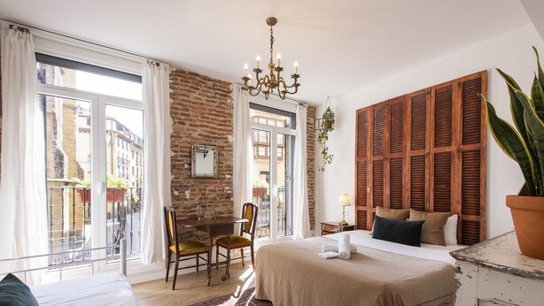 Un dormitorio con cama, escritorio, silla, candelabro y vista a la calle.