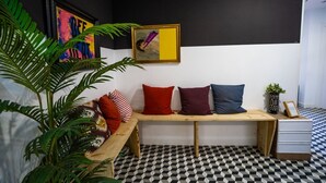 Una habitación con piso a cuadros, un banco de madera con cojines, un cuadro enmarco y una planta en maceta.