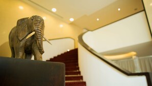 Una escultura de madera de elefante sobre una superficie oscura, cerca de una escalera con alfombra roja y barandilla de metal.