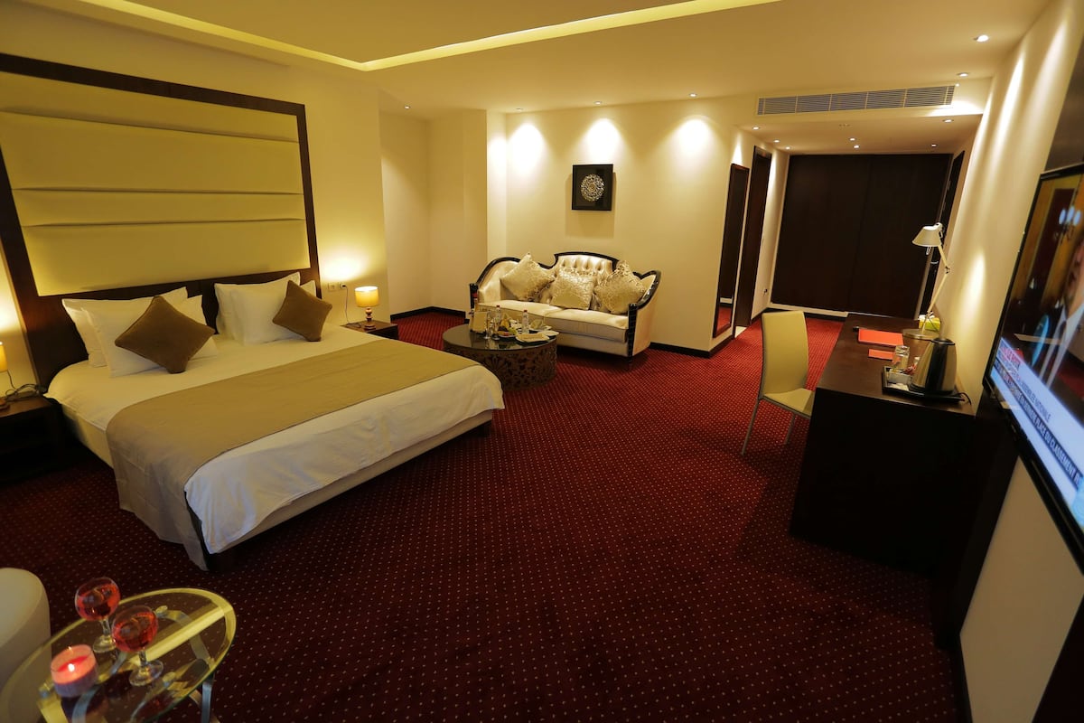 A hotel room with a large bed, a sofa, a small table with a candle, and a TV.