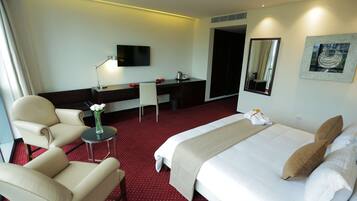 A hotel room with a bed, a desk, a chair, a TV, and a mirror.
