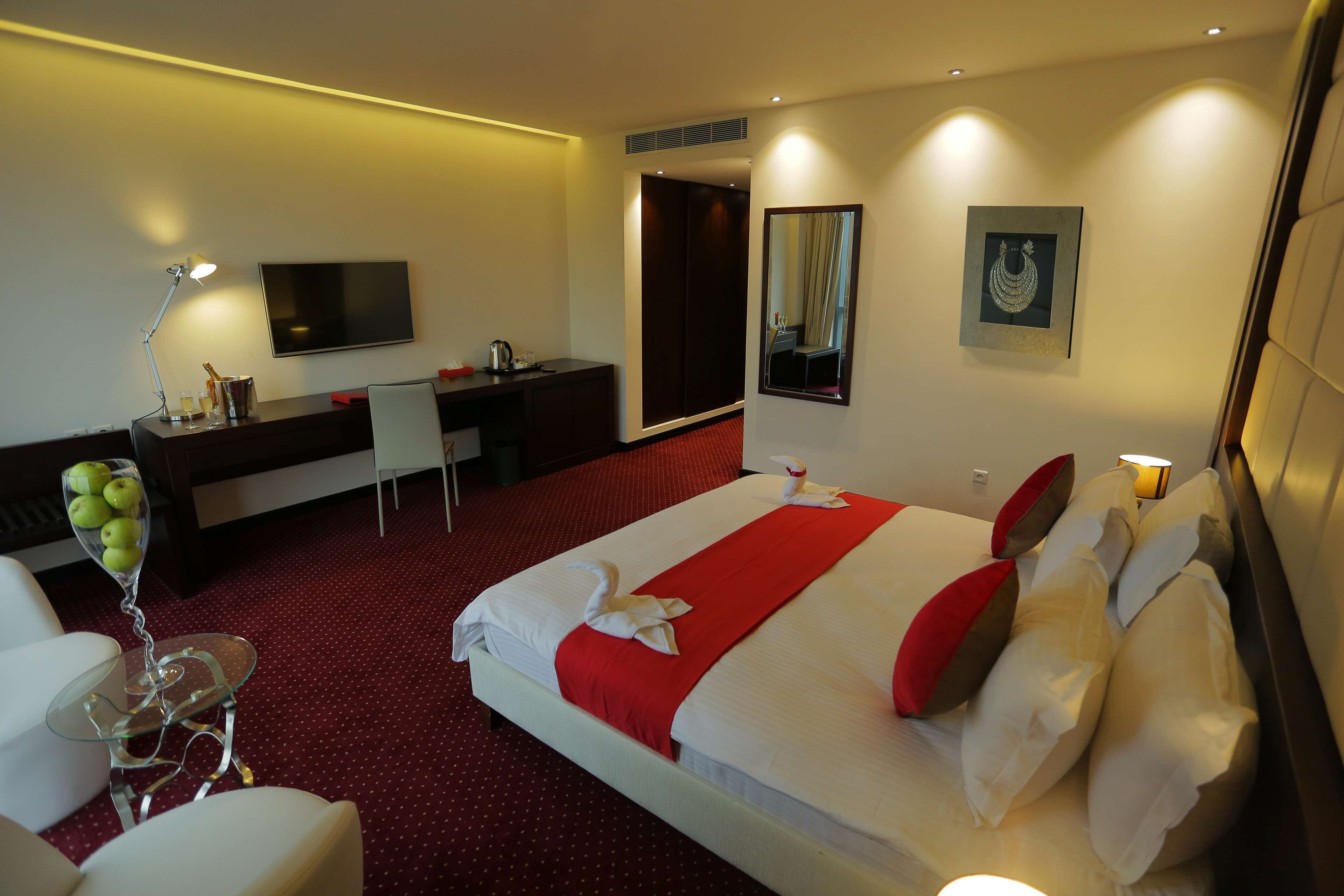 A hotel room with a bed, a desk, a chair, a TV, and a mirror.