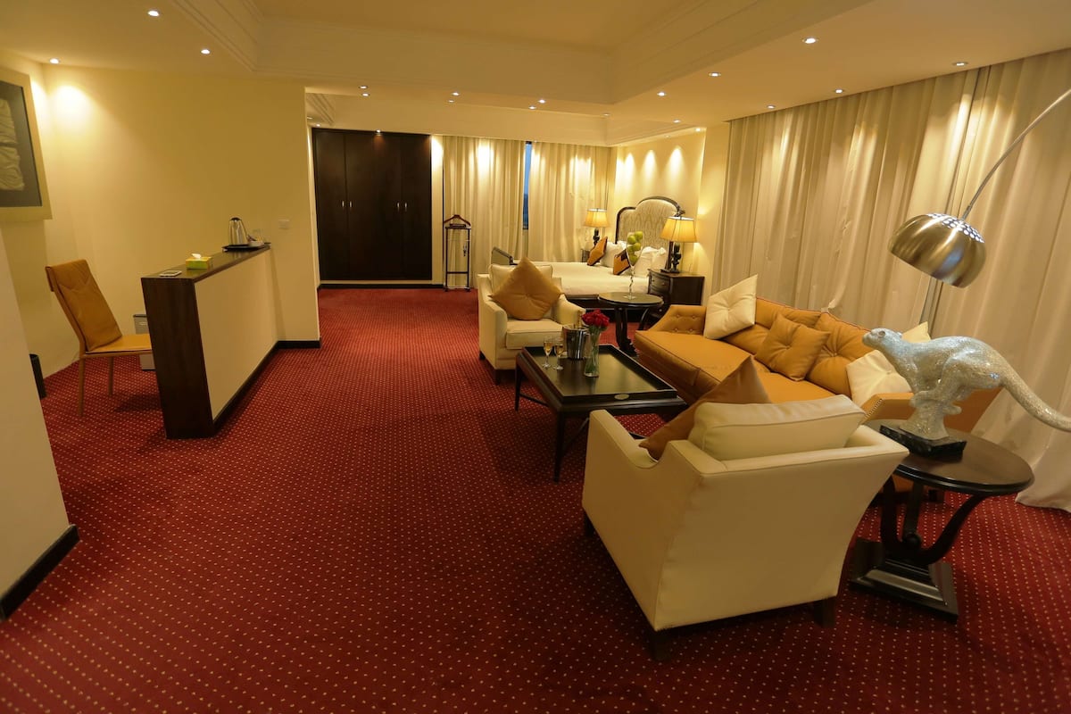 A hotel room with a red carpet, a sofa set, a coffee table, a lamp, and a decorative sculpture.