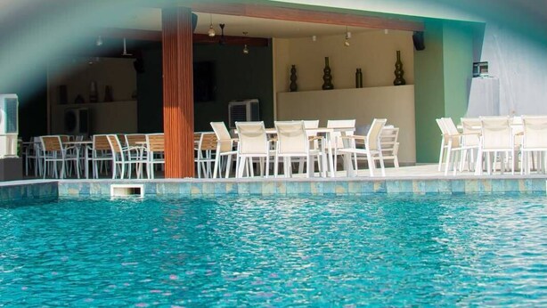 Una piscina con sillas y mesas de descanso, un edificio rojo al fondo y un diseño arquitectónico moderno.
