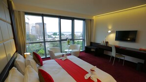 Habitación de hotel con una cama grande, un escritorio, una silla, un televisor y vistas de la ciudad.