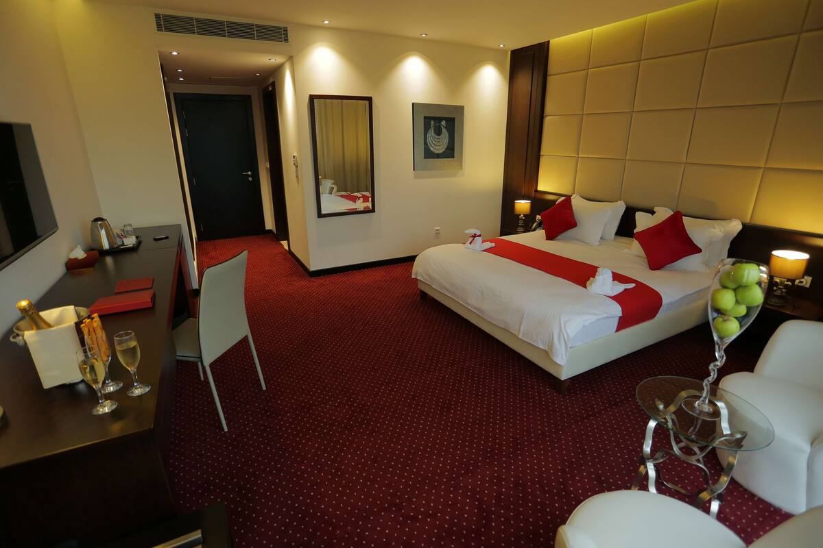 A hotel room with a large bed, a desk with a chair, a TV, and a minibar.