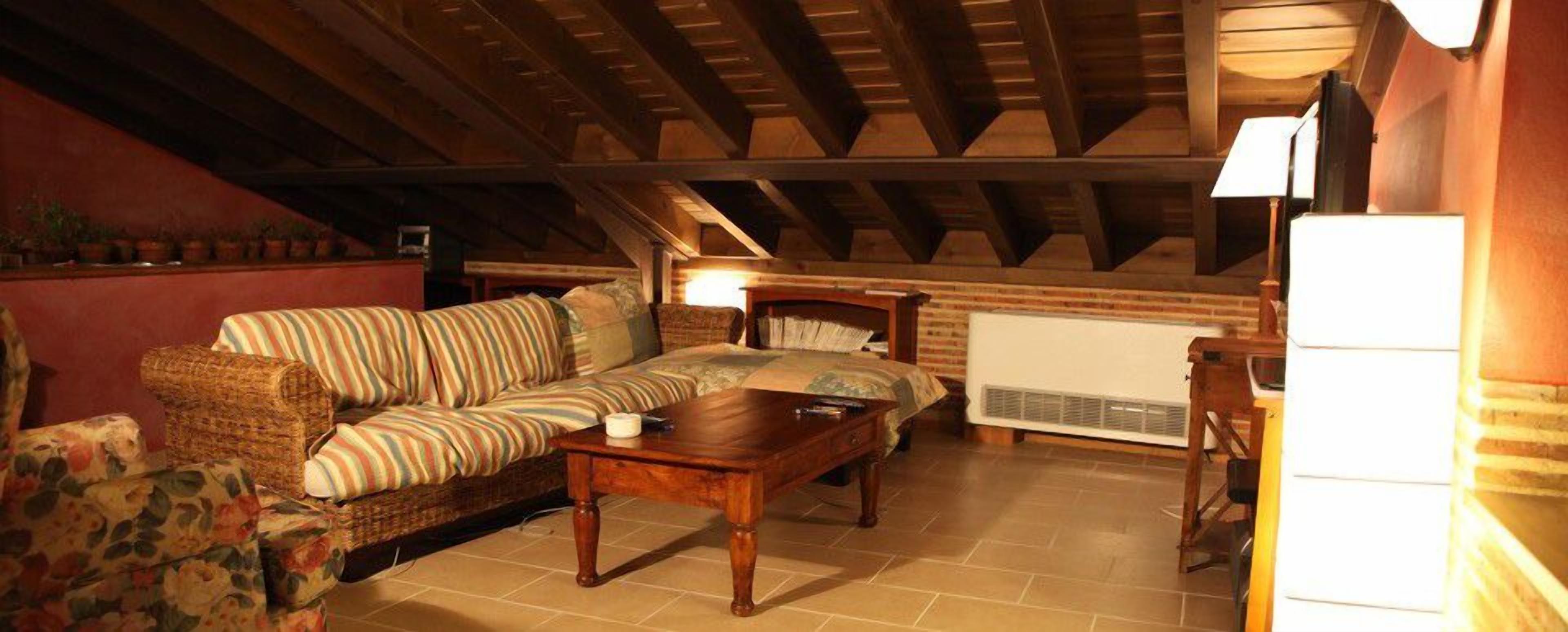 A cozy attic bedroom with a wooden ceiling, a bed, a sofa, and a radiator.