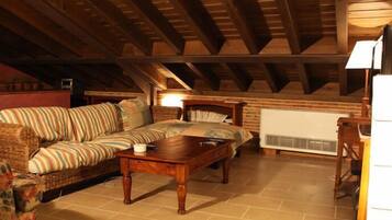A cozy attic bedroom with a wooden ceiling, a bed, a sofa, and a radiator.