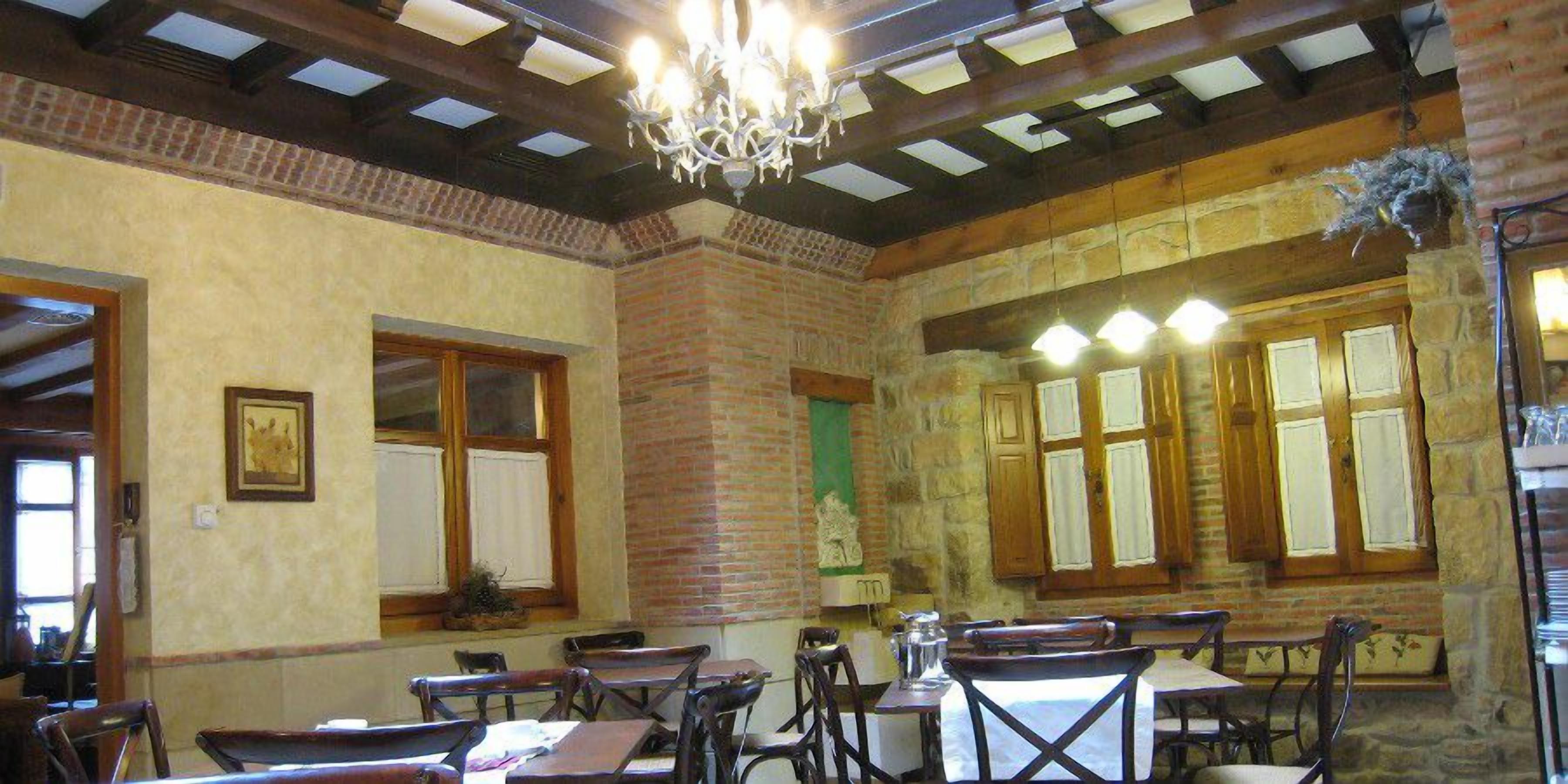 Un comedor con mesas y sillas de madera, una araña y paredes de piedra.