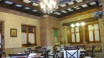 Un comedor con mesas y sillas de madera, una araña y paredes de piedra.