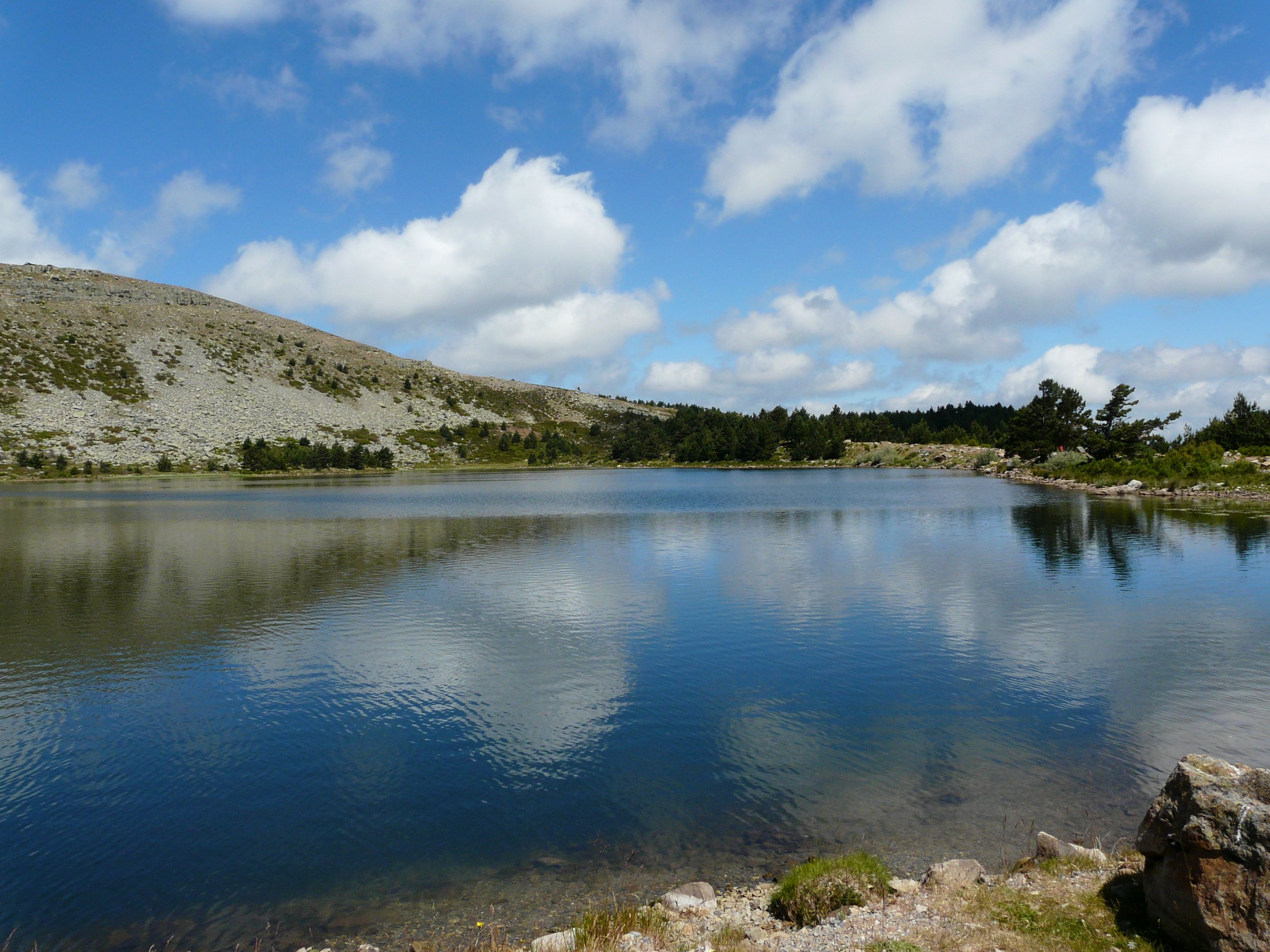 A calm lake with clear water, surrounded by rocky terrain and sparse vegetation.