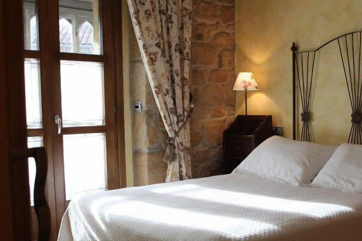 Un dormitorio con cama, dos lámparas de noche, una pared de piedra y una ventana con cortinas.