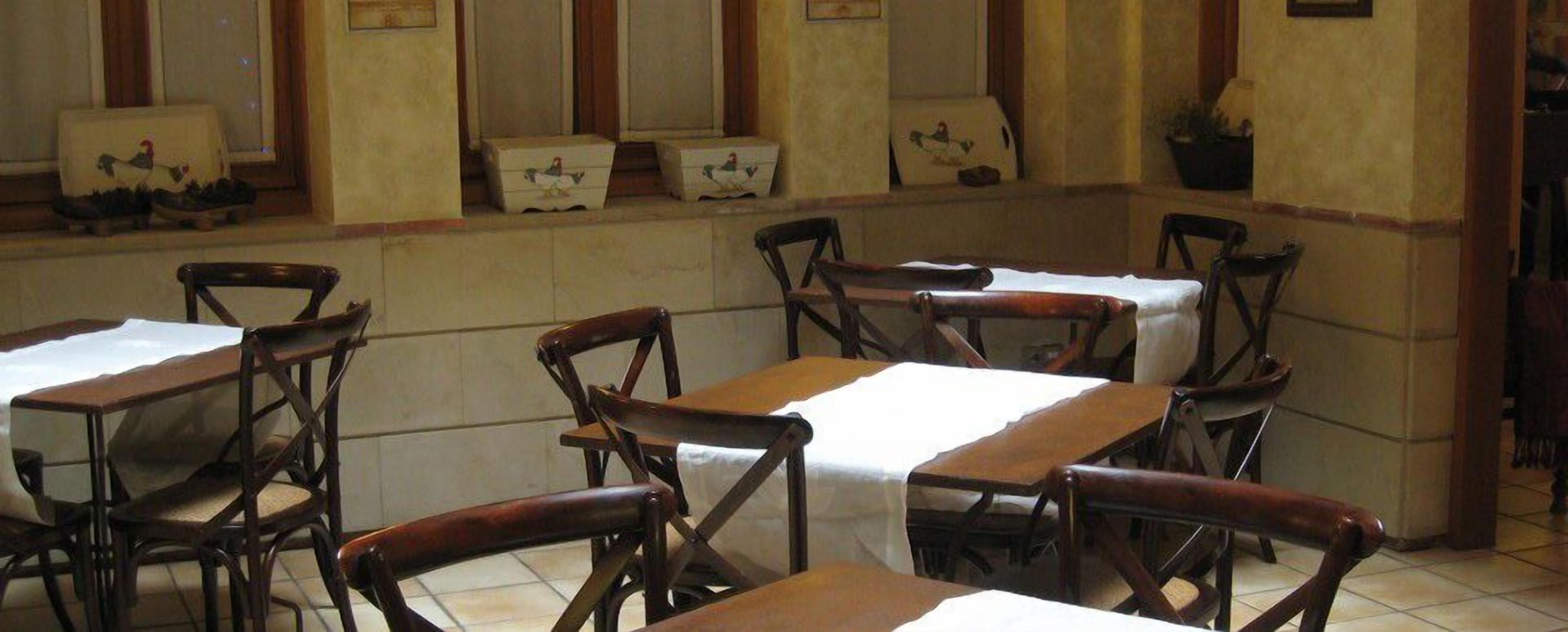 A dining area with wooden tables and chairs, each covered with a white tablecloth.