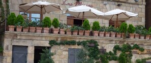 Un edificio con terraza al aire libre, sombrillas, plantas en macetas en el balcón y fachada de piedra.