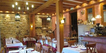 Um restaurante com paredes de pedra, vigas de madeira e mesas postas para refeições.