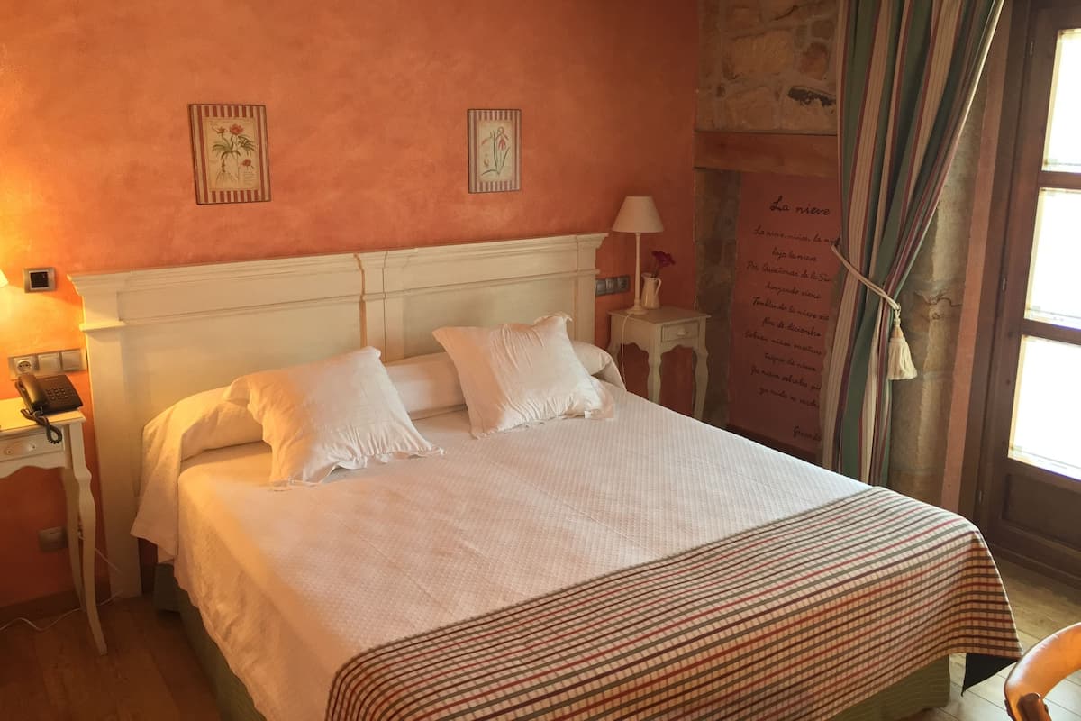 Una cama bien hecha con ropa de cama blanca, una mesita de noche con una lámpara e ilustraciones botánicas enmarcadas en la pared.