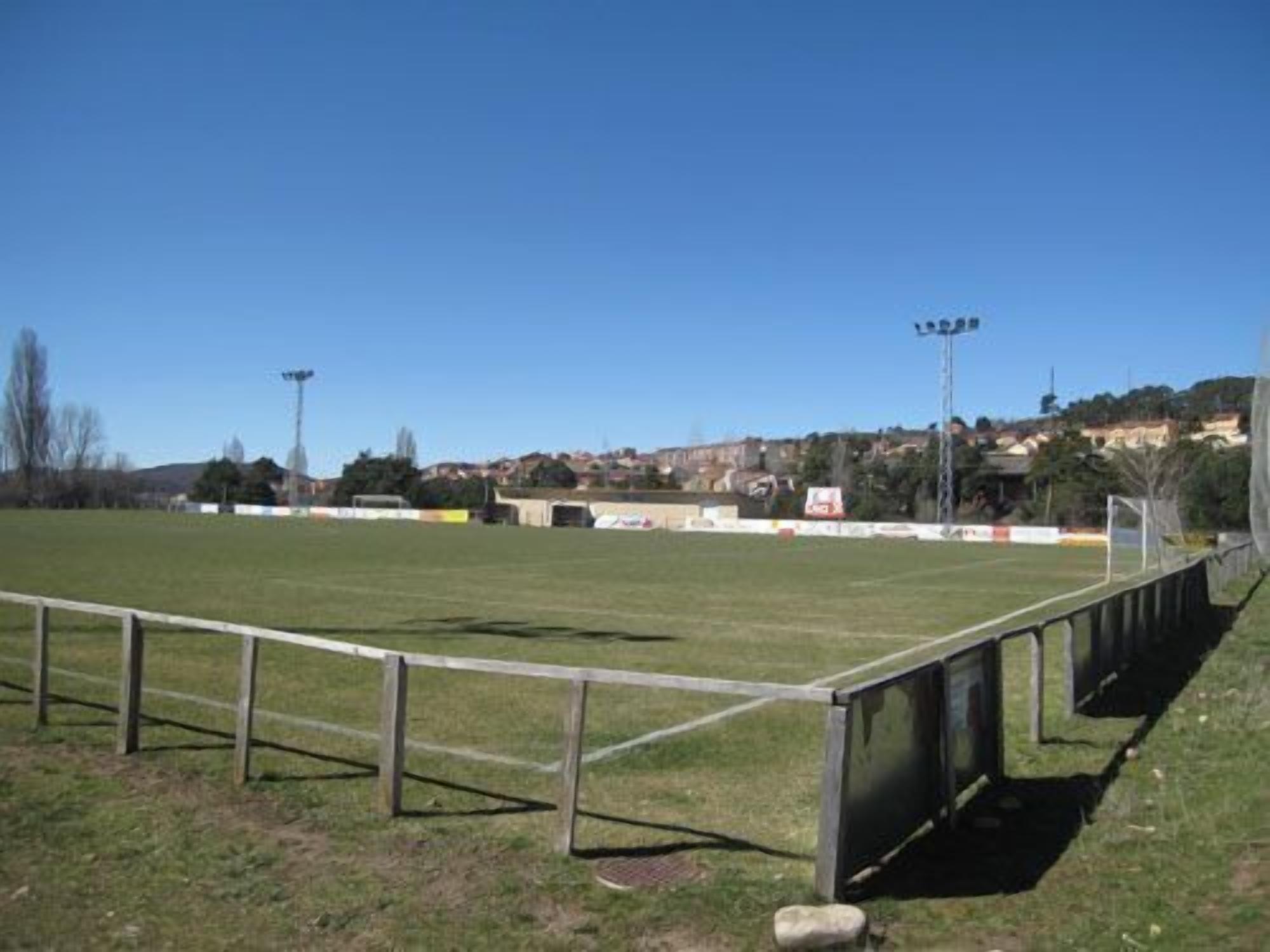 Un campo deportivo con vallas metálicas, postes de portería y focos.