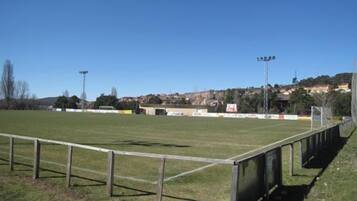 Un campo deportivo con vallas metálicas, postes de portería y focos.