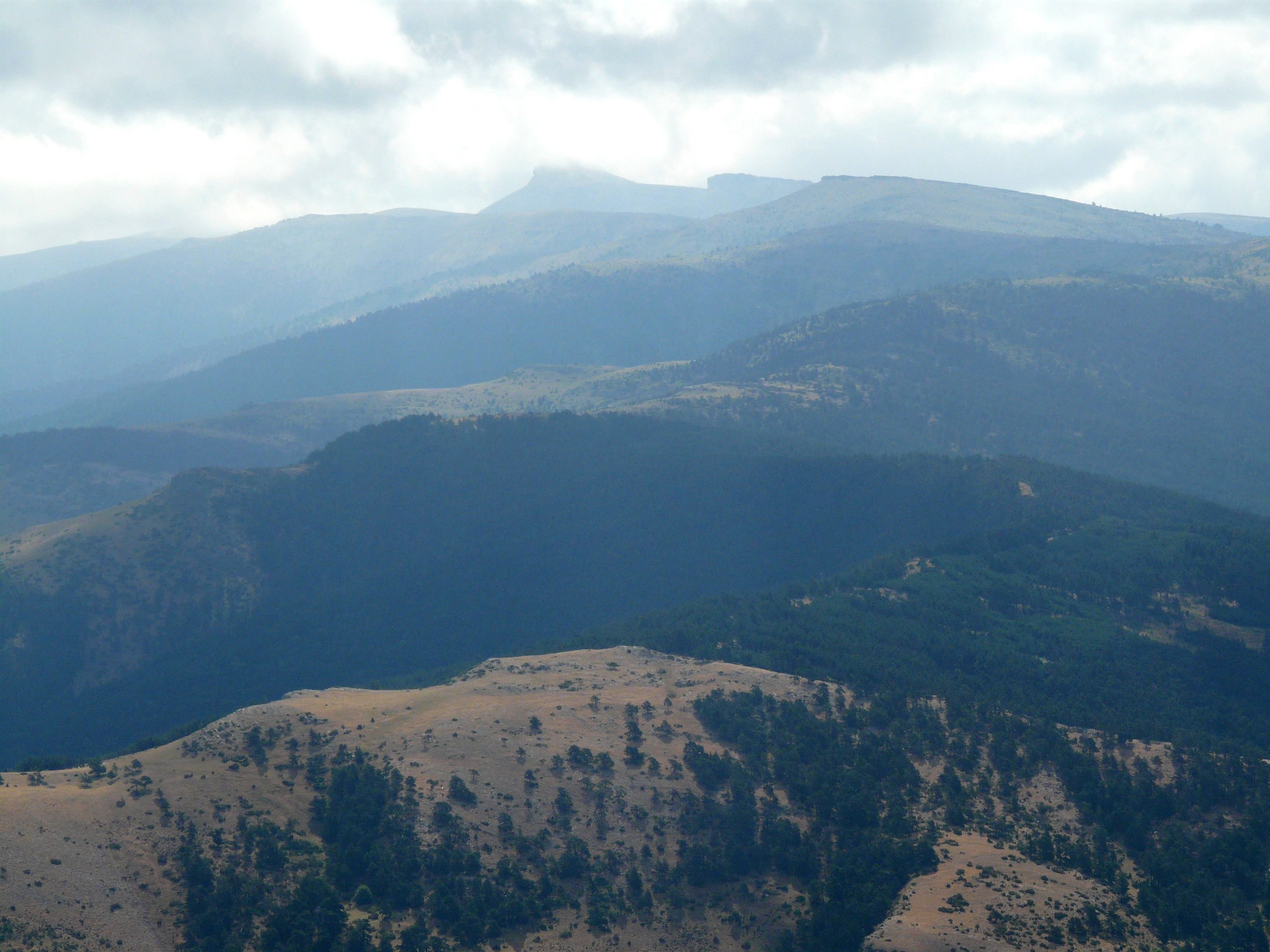 A panoramic view of a mountainous landscape with rolling hills and sparse vegetation.