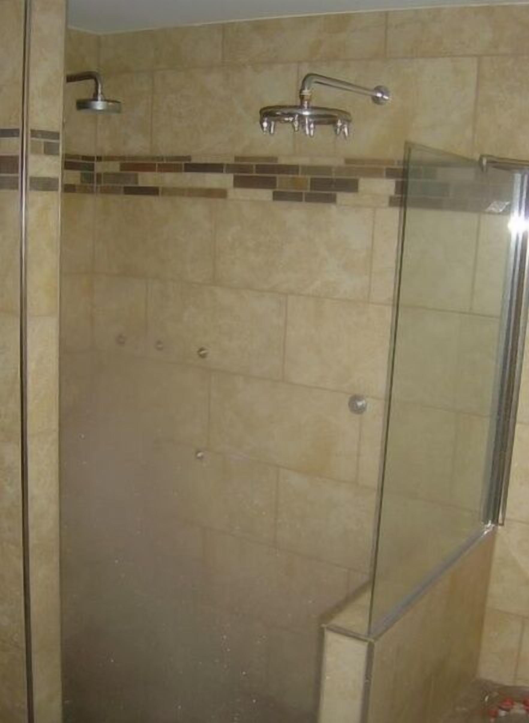 A glass-enclosed shower stall with a tiled wall and a showerhead.