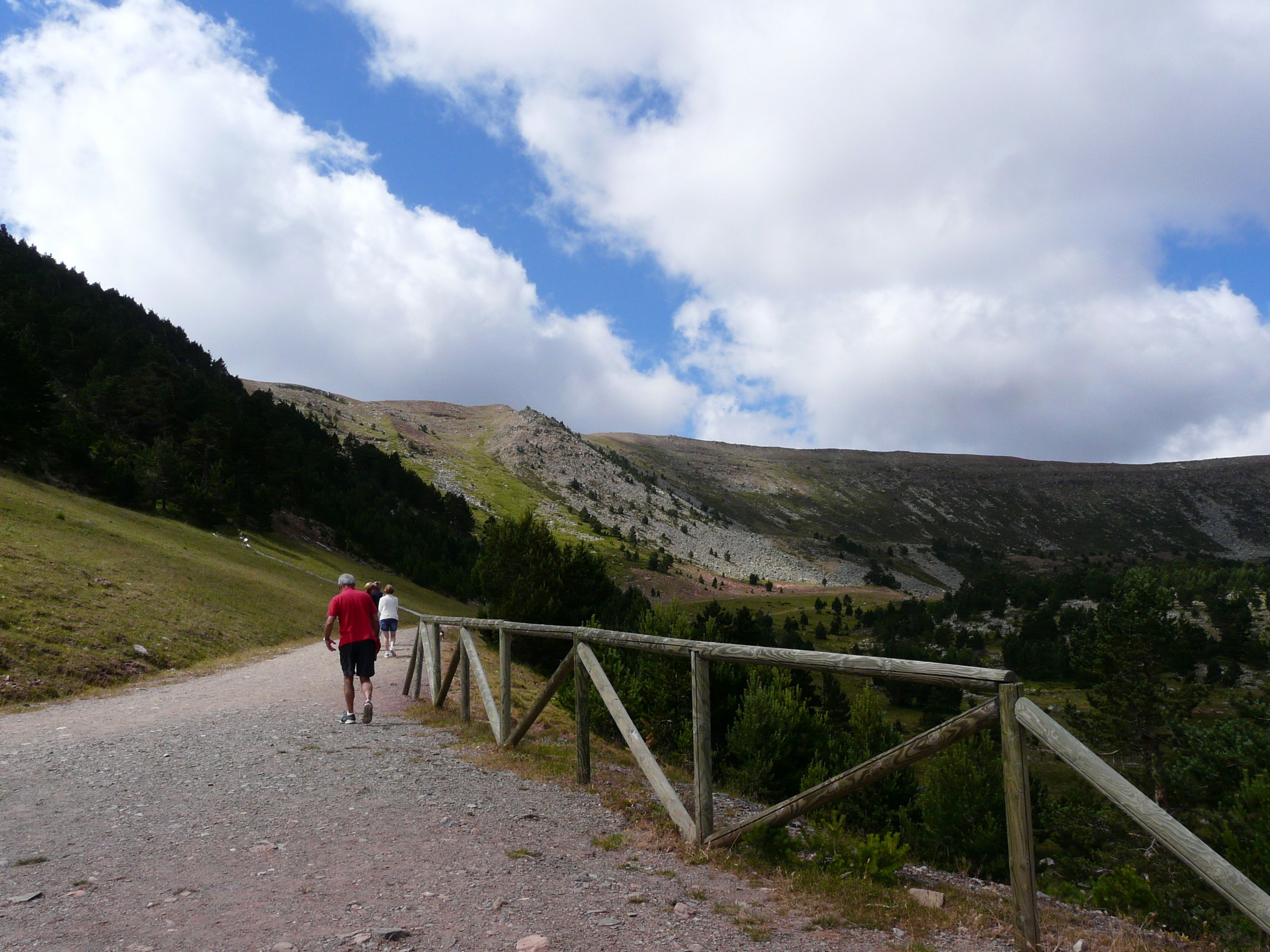 Un sentiero sterrato con ringhiere in legno che si snoda attraverso una zona montuosa.