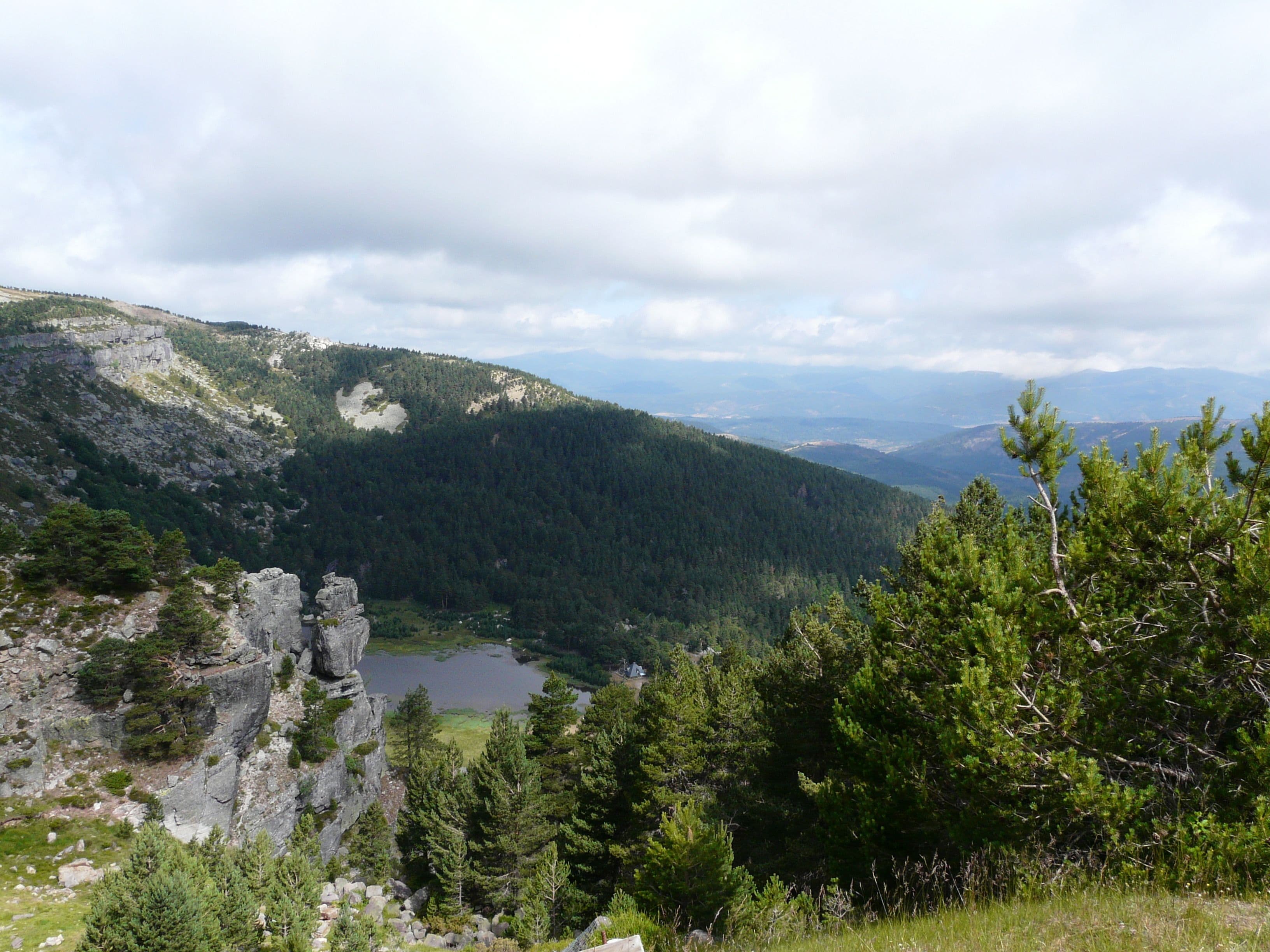 A mountainous landscape with a lake, dense forest, and rocky outcrops.