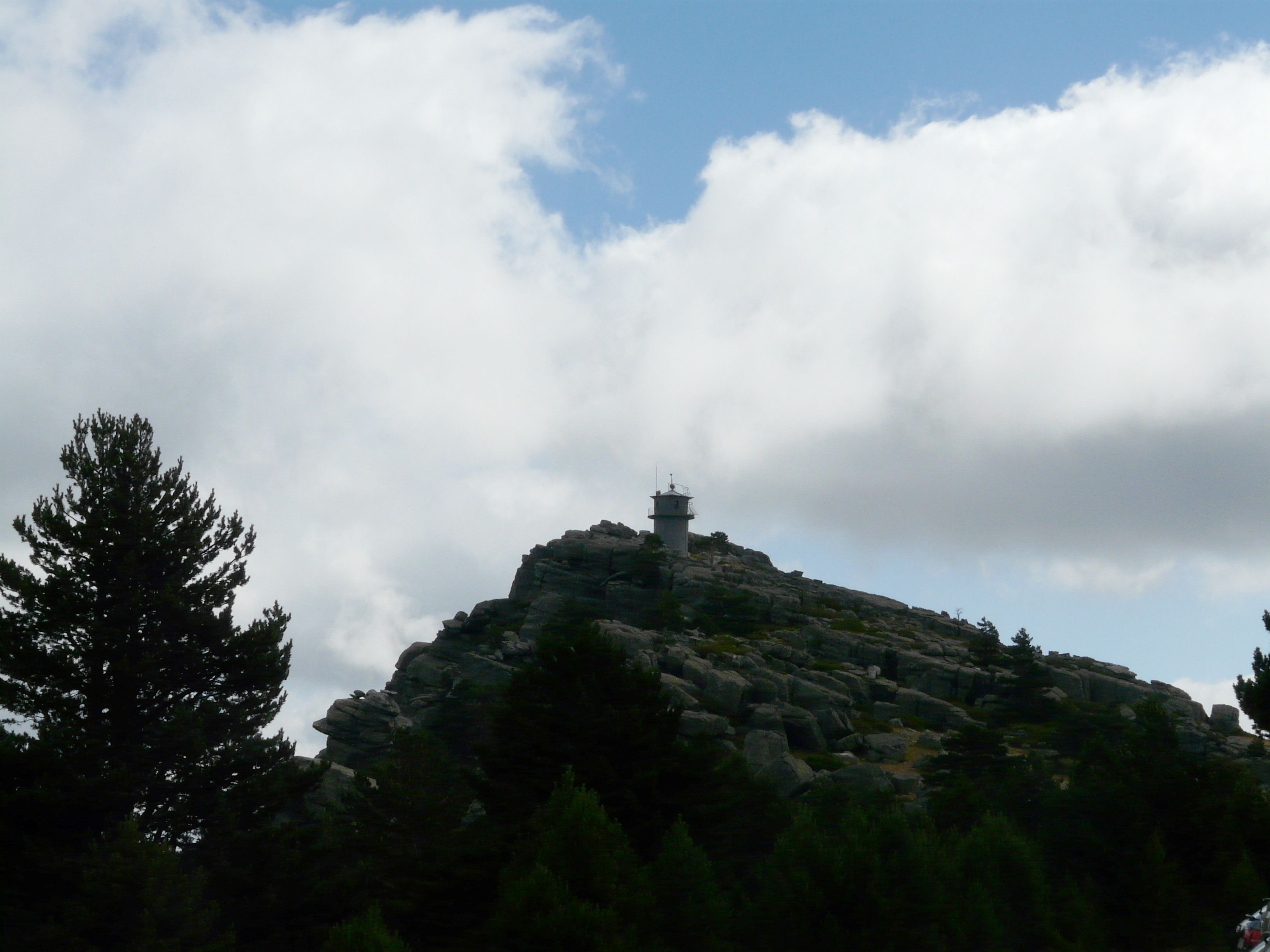 Una colina rocosa con una pequeña torre en la cima, rodeada de árboles.