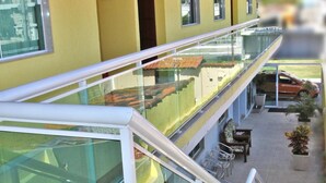 A modern building with a yellow exterior, a glass balcony with a white railing, and a car parked outside. - MDJ Suites (Cabo Frio)