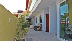 A hotel corridor with a reception desk, a seating area with chairs, and potted plants. - MDJ Suites (Cabo Frio)