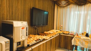 A buffet setup with various food items, a microwave, and a television on the wall. - MDJ Suites (Cabo Frio)