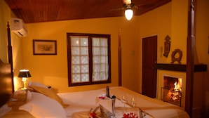 Una cama impecable con una bandeja de champán, copas y flores, una chimenea y un cuadro en la pared.