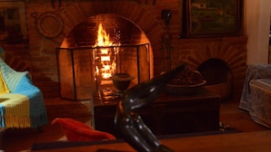 Una habitación acogedora con chimenea de ladrillo, una mesa con un cuenco de fruta y una manta colorida en una silla.