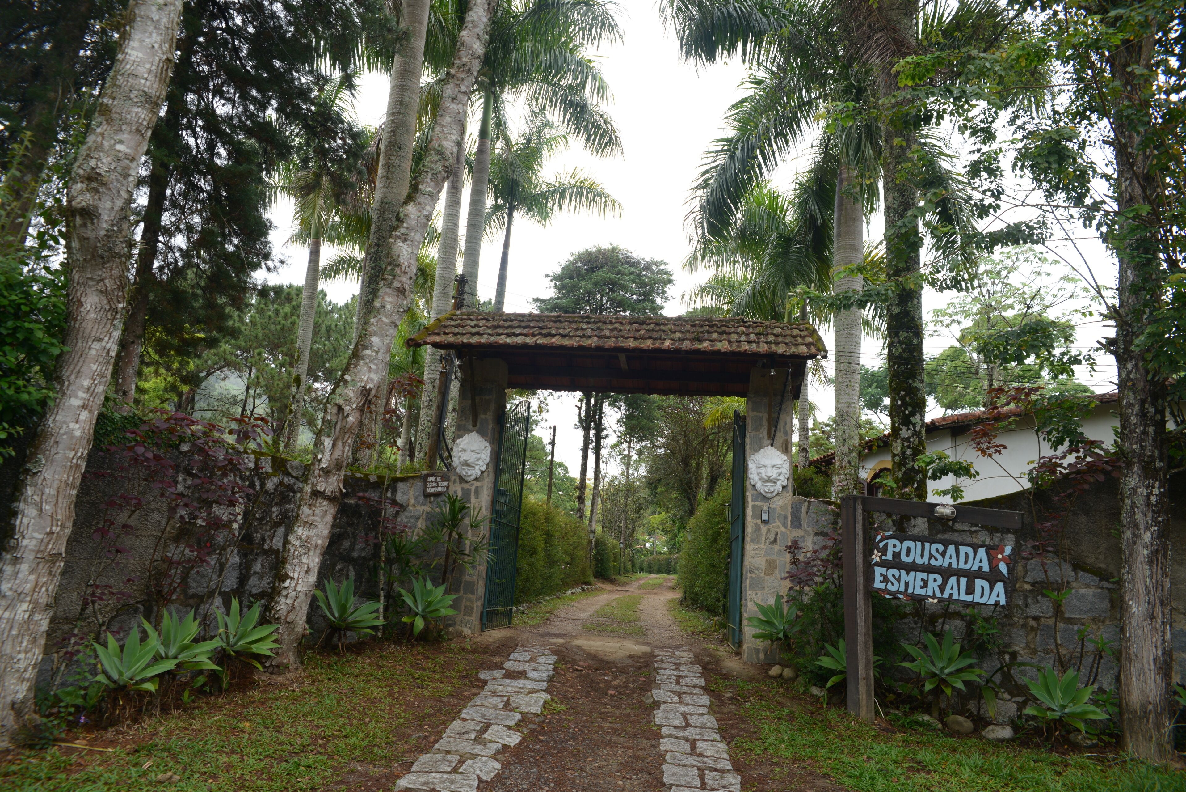 A stone pathway leading to a wooden archway with a sign reading "Pousada Esmeralda".