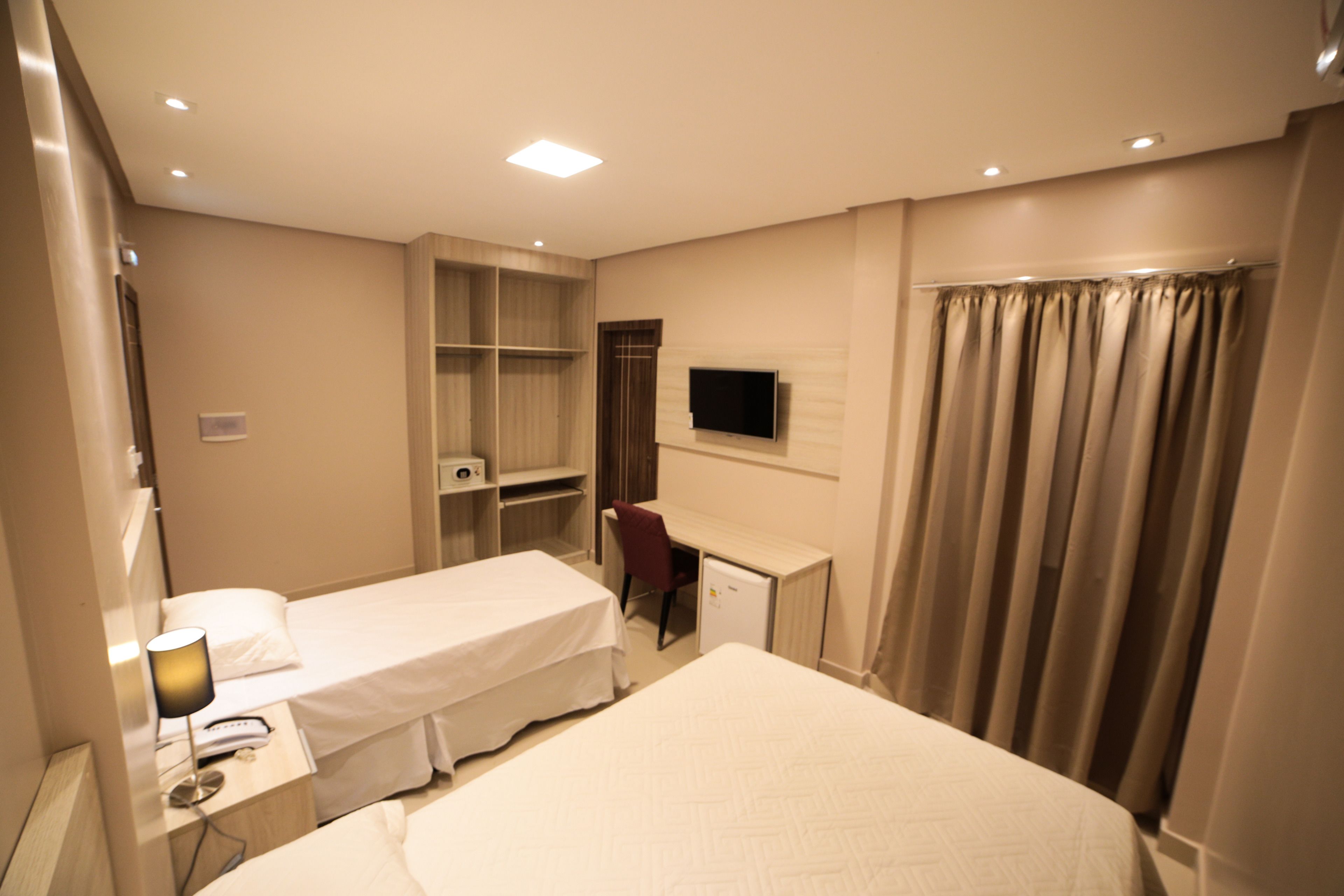 Une chambre d’hôtel avec deux lits simples, un bureau avec une chaise, une télévision, une armoire et un rideau de douche.