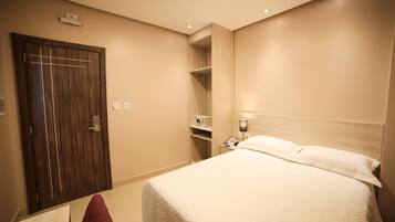 A hotel room with a wooden wardrobe, a bedside table with a lamp, and a bed with white bedding.