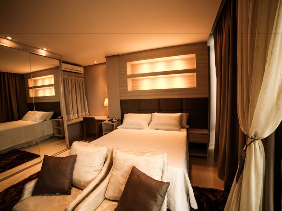 A hotel room with a large bed, a desk, a chair, and a mirror.