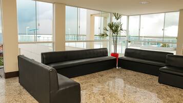 Ett modernt väntrum med svarta lädersoffor, en krukväxt och stora fönster som ger utsikt över omgivningen.