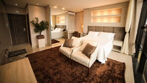 A modern hotel room with a large bed, a sitting area with a chair, a small table, and a potted plant. - Hotel London Santarem (Santarém)