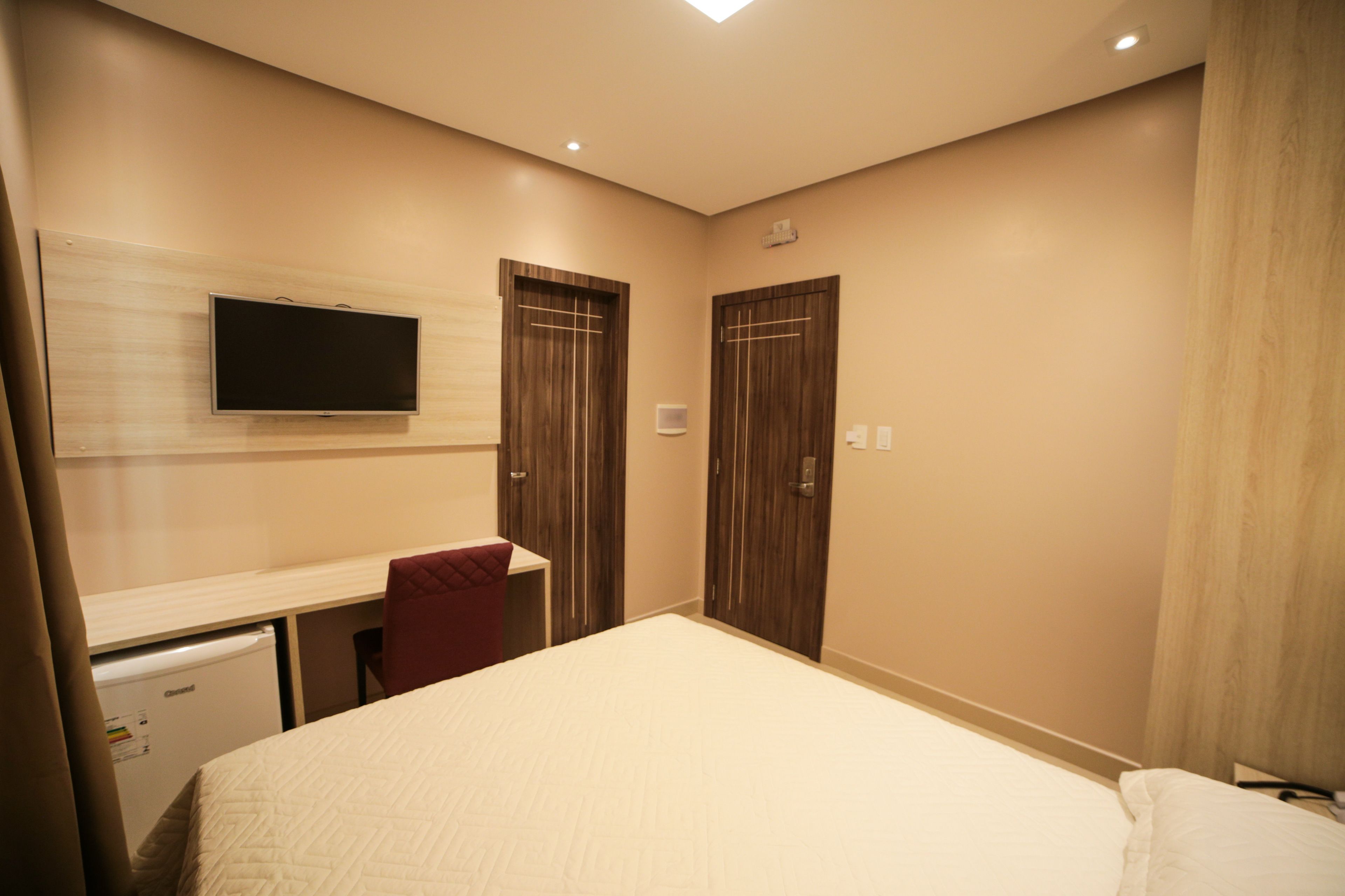 Een hotelkamer met een bed, een bureau, een aan de muur bevestigde televisie en een kledingkast.