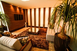 Una sala de estar moderna con un televisor de pantalla plana montado en la pared, una mesa de centro de vidrio y varios sofás con cojines estampados.