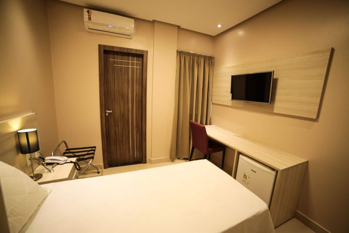 A hotel room with a bed, desk, chair, TV, and a small refrigerator.