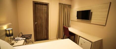 A hotel room with a bed, desk, chair, TV, and a small refrigerator.