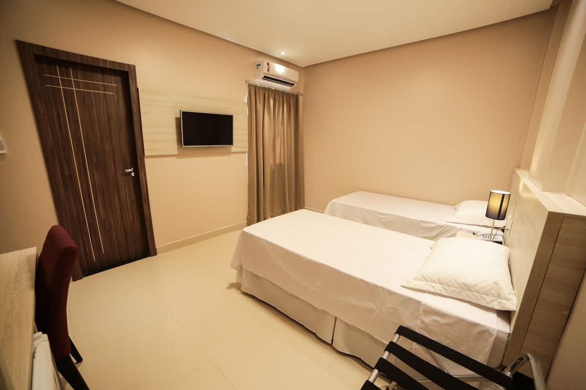A hotel room with two beds, a TV mounted on the wall, an air conditioning unit, and a wooden door.