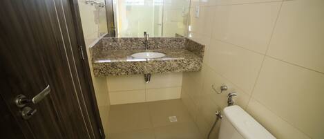 A bathroom with a granite countertop sink, a toilet, and a shower area.