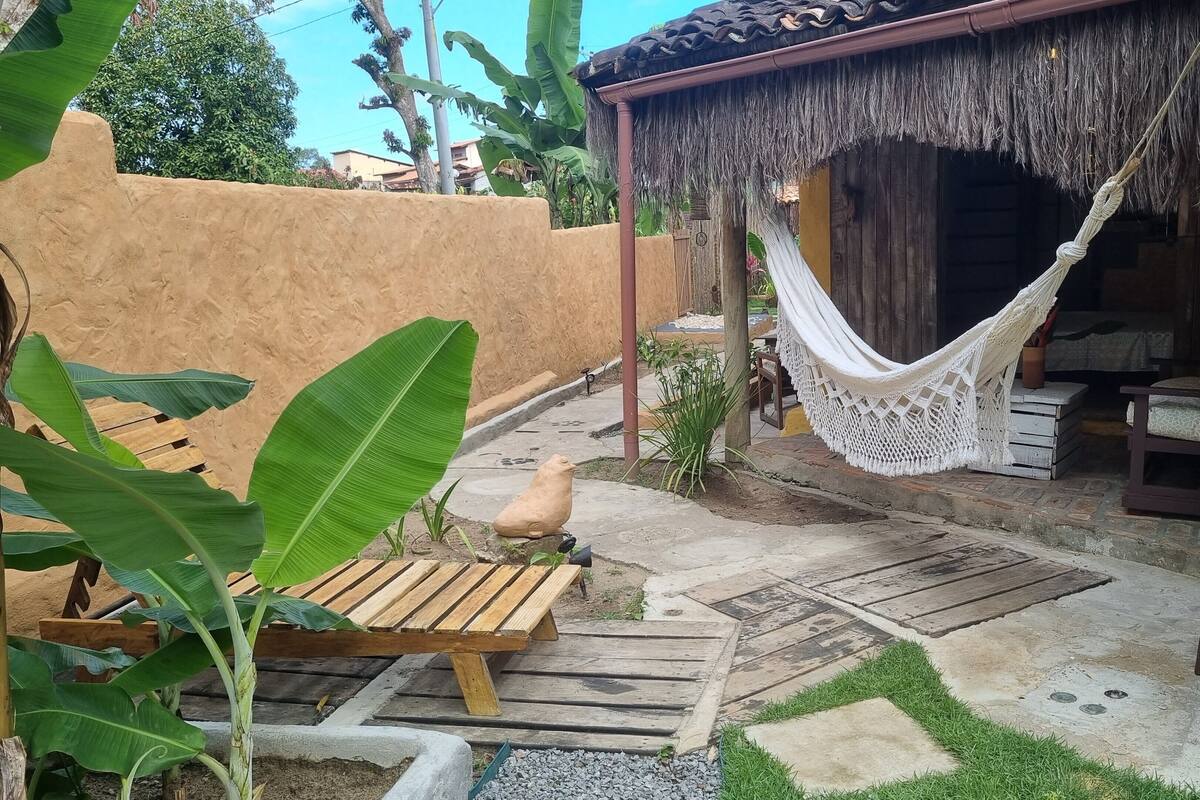 Una hamaca bajo un techo de paja, un banco de madera y un sendero de piedra.