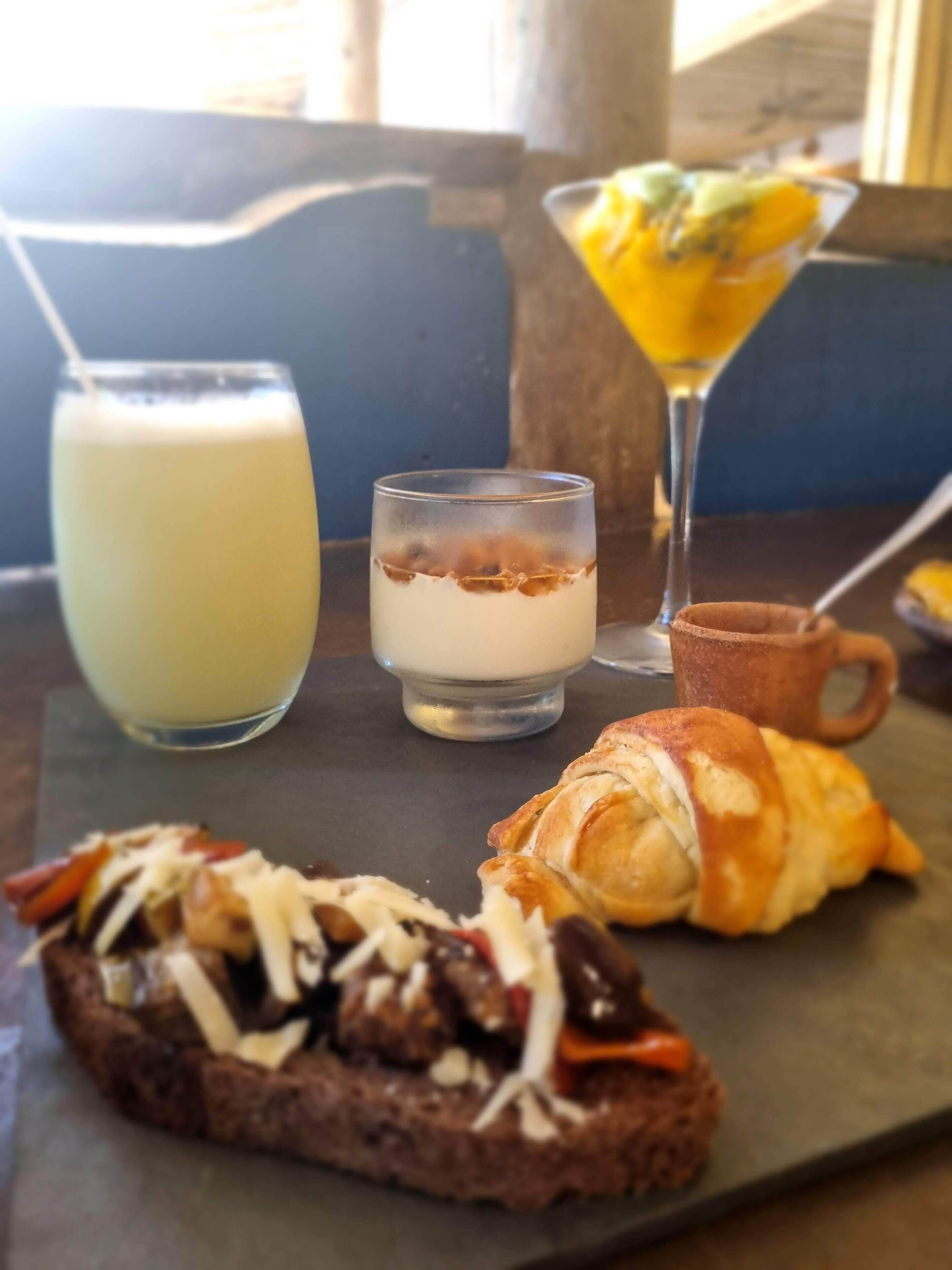 A meal with a croissant, a sandwich, a drink, and a dessert on a slate board.